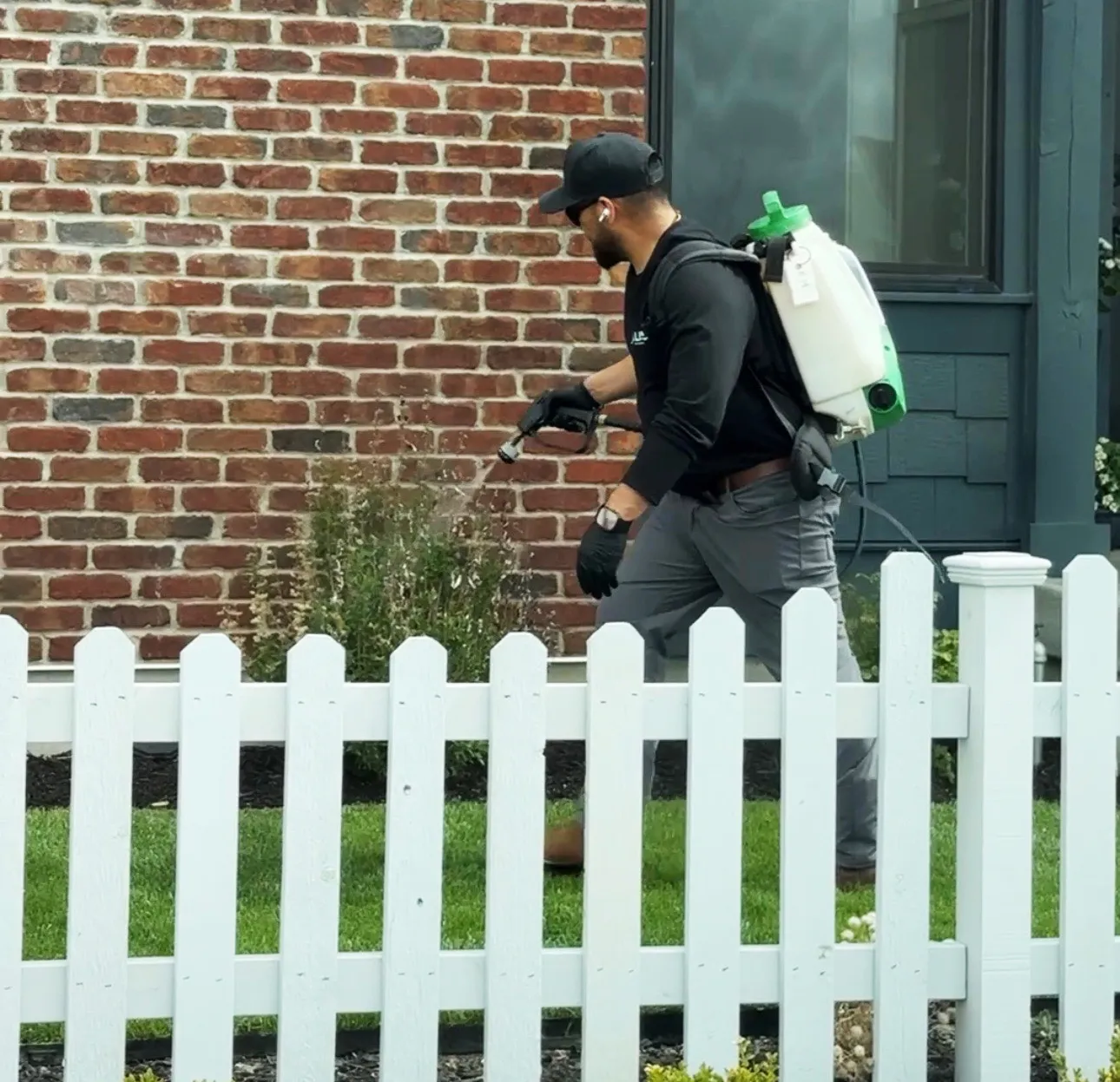 Technician with a backpack sprayer treating a brick home's exterior, exterior pest control in Salt Lake City