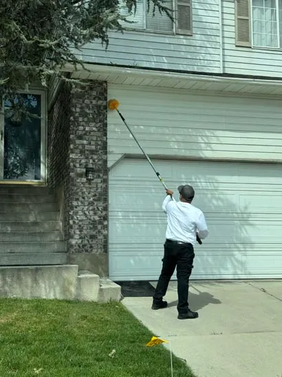 Salt Lake City pest control technician treating eaves above a garage door with an extension pole