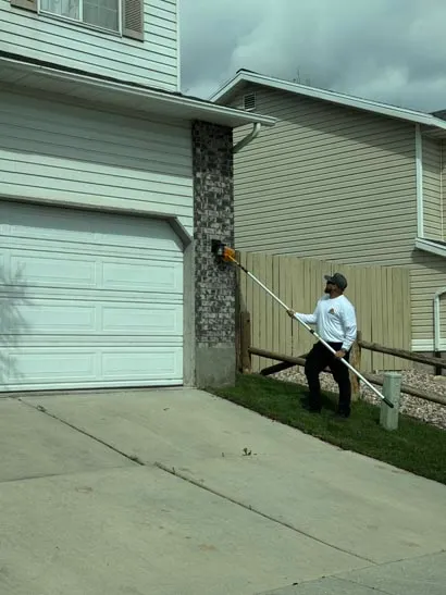 Salt Lake City pest control technician treating the eave above a garage with an extension pole