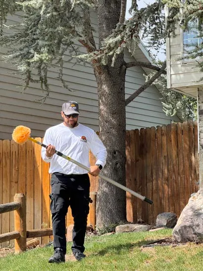 Bliss technician spraying the base of a tree in a fenced backyard, Salt Lake City exterior treatment