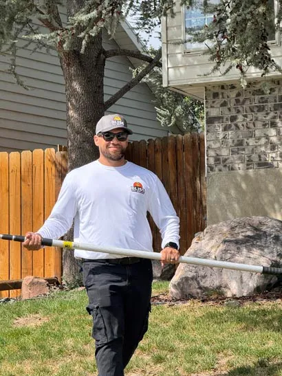Technician treating a tree trunk and fence line with a spray wand, yard pest control in Salt Lake City
