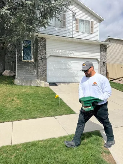 Bliss technician carrying treatment equipment across a front yard, Salt Lake City pest control