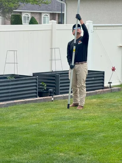 Salt Lake City pest control technician working an extension pole near a backyard fence