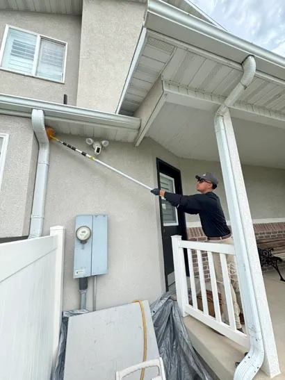 Bliss technician clearing webs from home eaves near a side door, Salt Lake City exterior treatment