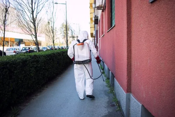 Technician in protective gear spraying along a building exterior, professional pest control in Salt Lake City